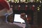 Back view of angry man freelancer in santa claus hat, raising and swinging fist on laptop screen sitting near christmas tree