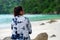 back view. asia woman wearing sunglasses and indigo shirt sitting on rock. front of her are sea and green forest. this image for