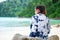 back view. asia woman wearing sunglasses and indigo shirt sitting on rock. front of her are sea and green forest. this image for