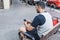 Back view of an athlete writes something on his mobile phone, while sitting on a sidewalk bench