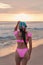 Back view of an attractive latina woman wearing a pink summer bikini and bandana in a beautiful sunset on the seashore