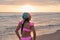 Back view of an attractive latina woman wearing a pink summer bikini and bandana in a beautiful sunset on the seashore