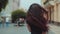 Back view of attractive long-haired curly brunette woman walking down the city-street or alley, turns to camera and