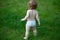 Back view of baby standing barefoot on the green lawn. Happy childhood and child healthcare. Kids growing.