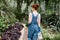 Back view of beautiful caucasian woman in jeans overalls walking with water can in nursery. Female gardener watering