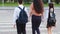 Back view from behind woman mother with two children pupils girl and boy with backpacks holding hands stepping walking