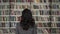 Back view of black hair woman pointing at a book on a bookshelf