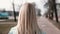 Back view blonde woman walking and looking left. Caucasian girl in blue coat with beautiful long fair hair. Slow motion.