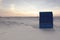 Back view of blue roofed wicker beach chair on empty sand beach at sunset time. Colorful sky