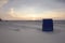 Back view of blue roofed wicker beach chair on empty sand beach at sunset time. Colorful sky