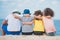 back view of boys and girls sitting together on wooden trunk at seaside