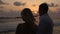 Back view of bride and groom enjoying sunset on tropical beach near balustrade on vacation. Newlyweds hugging and