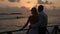 Back view of bride and groom enjoying sunset on tropical beach near balustrade on vacation. Newlyweds hugging and