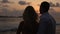 Back view of bride and groom enjoying sunset on tropical beach near balustrade on vacation. Newlyweds hugging and