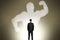 Back view of businessman with strong muscle shadow standing on wall background. Confidence and strength concept