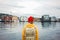 Back view of carefree man traveller with touristic rucksack wearing yellow coat and rad hat standing on berth and looking toward s