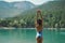 Back view carefree woman in swimsuit posing with raised hands up on background of mountain lake and mountains in the