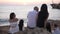 Back view of Caucasian carefree family admiring sunset on Mediterranean sea coast talking. Happy relaxed father mother