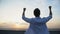 Back view of Caucasian man raising hands to sky on sunset background, motivation