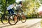 Back view of a couple of fashionable sportsmen, a male and female, riding their bicycles in the city park, staying fit and sporty