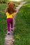 Back view. curly smiling girl in a yellow T-shirt holds a large brown teddy bear on her neck and runs along the path