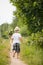 Back view on cute bare feet kid boy in straw hat running on a countryside road and holding bunch of wild flowers