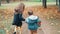 Back view cute brother and sister little boy and girl running holding hands with their toys through autumn alley slow mo