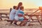 Back view of a cute family - mother with her sons sitting on a bench and looks at the bright sunset on the seacoast.