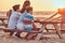 Back view of a cute family - mother with her sons sitting on a bench and looks at the bright sunset on the seacoast.