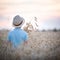 Back view on cute kid boy in straw hat walking in the wheat field on beautiful sunset. Child on the meadow