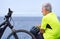 Back view of cyclist man resting at sea on the cliff after activity with his electro bike. Standing with helmet in the hand