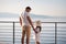 Back view of daughter with her father stand on heigh balcony in front of sea sunset. Dad with his little girl looking on