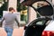 Back view of delivery man takes out large festive white box with beautiful red bow from trunk of car