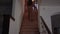 Back view of eerie woman walking up the stairs slowly and entering room in house. Brunette barefoot witch indoors. Magic