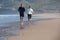 Back view of elderly couple running barefoot on sea beach