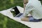 Back view of faceless young man concentrated using the computer sitting outdoor under a tree