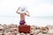 back view of fashionable tourist in striped swimsuit and hat sitting on retro travel bag