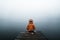 Back view of fashioned young woman sitting on wooden dock looking at view on a misty morning.