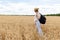 Back view of female agronomy with travel backpack walking at path in middle of wheat fields exploring international