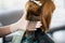 Back view of a female hairdresser doing a hairstyle for a redhead in a beauty salon.The process of styling hair in the hair salon.