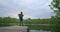 Back view: A female traveler with a backpack enjoys the beauty of a mountain forest lake standing on a wooden pier. Slow