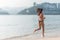 Back view of fit slim girl running barefoot on seashore wearing bikini. Young woman doing cardio exercise beach lit in