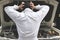 Back view of frustrated stressed young mechanic man in white uniform touching his head with hands against car in open hood at the