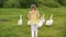 Back view of girl chasing white geese in countryside