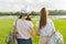 Back view, girl friends are walking in the park in nature. Girls walk along the green lawn, talk, have fun.