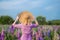 Back view. girl in a purple dress and a large wide-brimmed straw hat walks in a lupine flower field