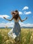 back view of a girl standing in a flower grass field with open arms freedom and fresh air blue sky