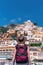 Back view of a girl in a white dress, a hat stands on the beach in Positano. View of houses and hotels in the background. Travel