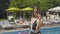 Back view of gorgeous confident woman standing in front of swimming pool and turning to camera. Portrait of beautiful