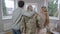 Back view of grey-haired army man in camouflage standing with wife and adult son at home looking out the window